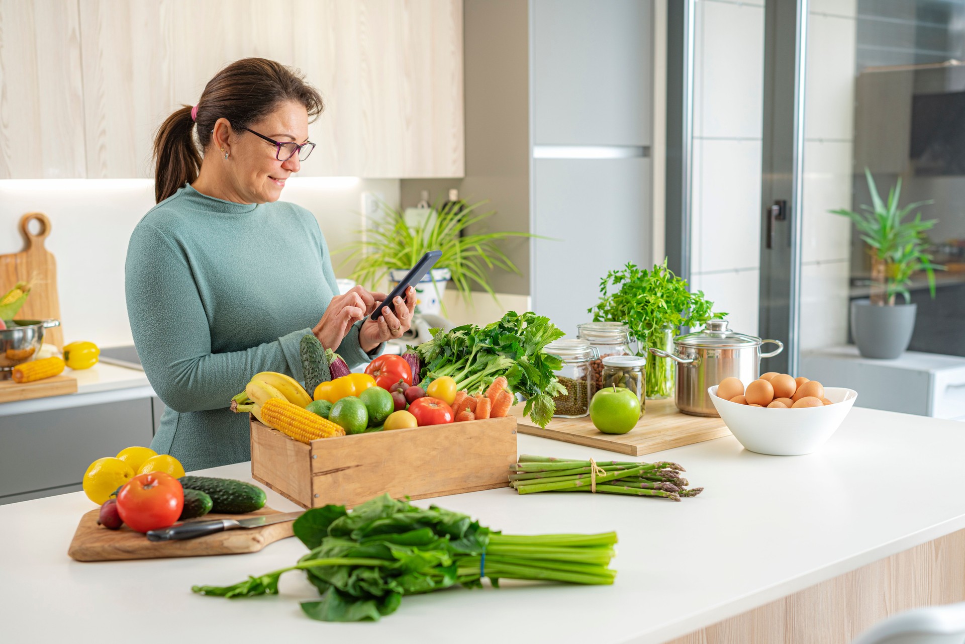 Femme dans la cuisine utilisant un smartphone pour vérifier les fruits et légumes livrés à domicile